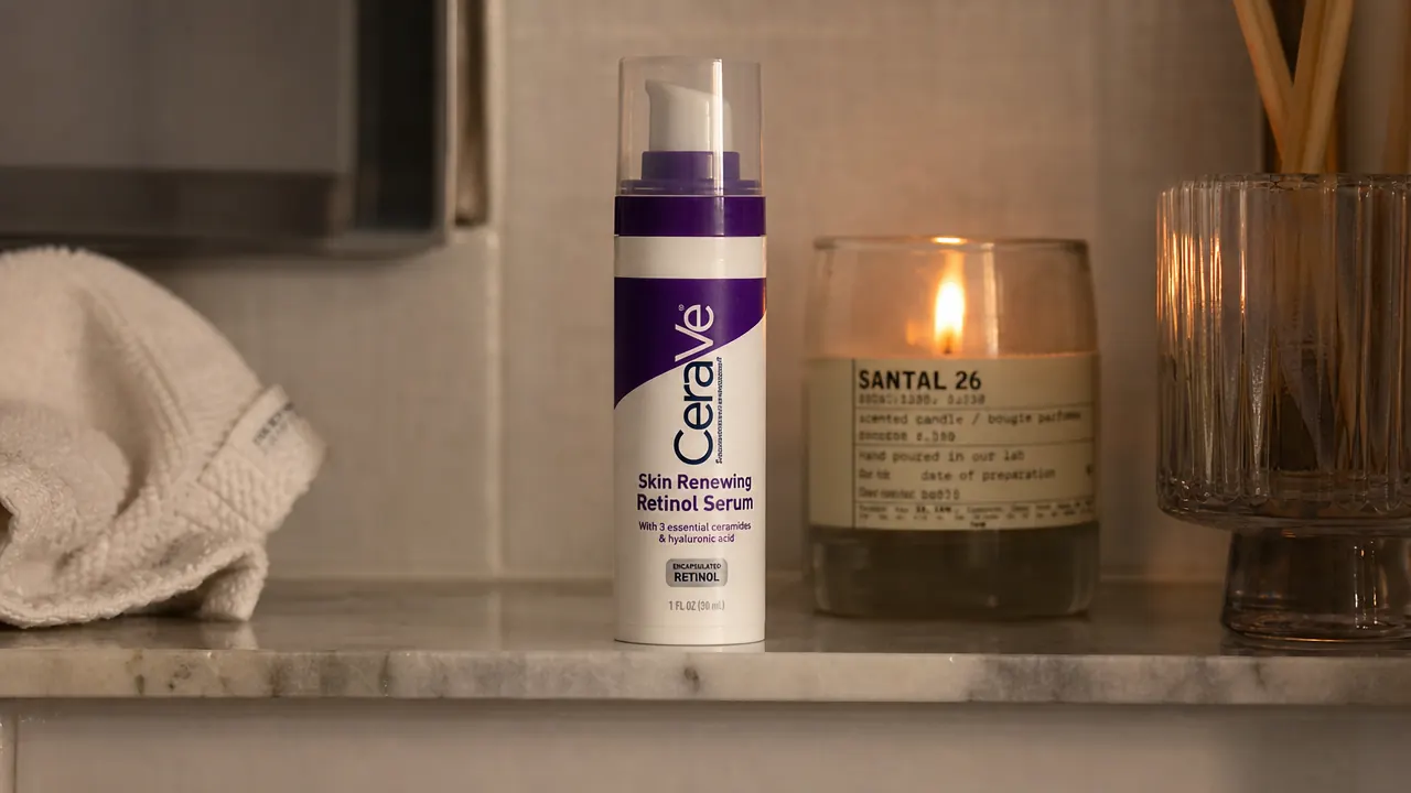 Bottle of CeraVe Anti Aging Retinol Serum on a bathroom shelf next to a glass of water and a white towel in soft evening light