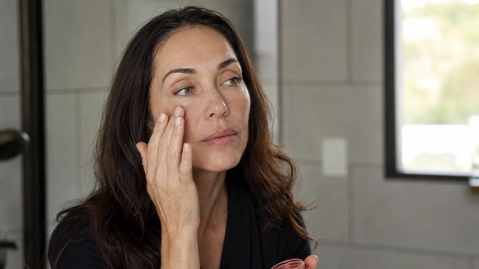 Woman applying tinted sunscreen in morning bathroom light, warm natural glow on skin
