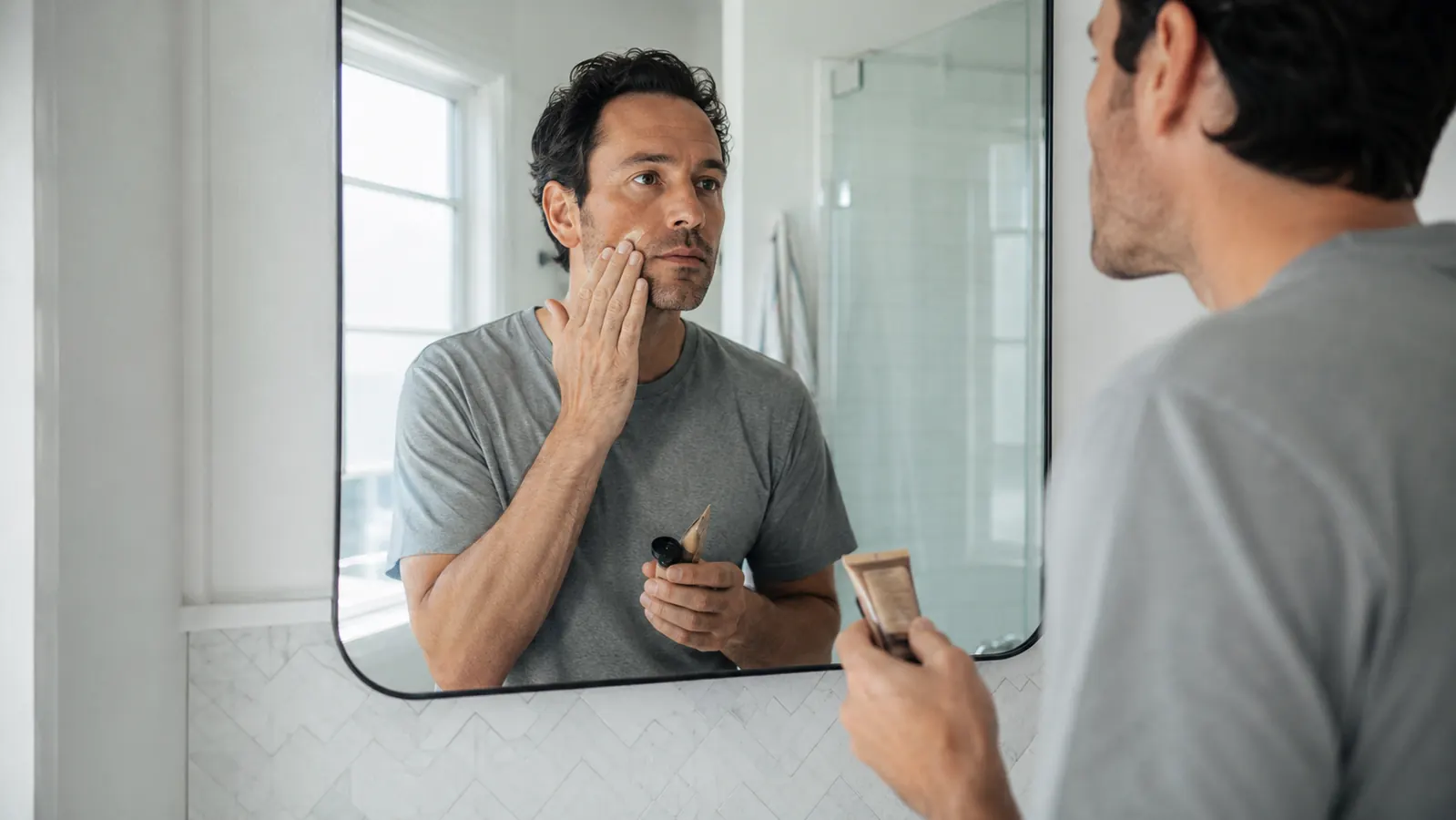 Man applying tinted sunscreen to his face in bathroom mirror morning light