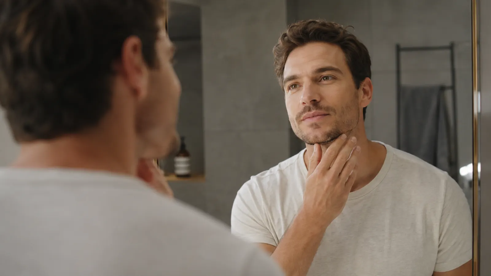 Man in his 30s looking in a mirror with clear, calm skin, bright bathroom lighting
